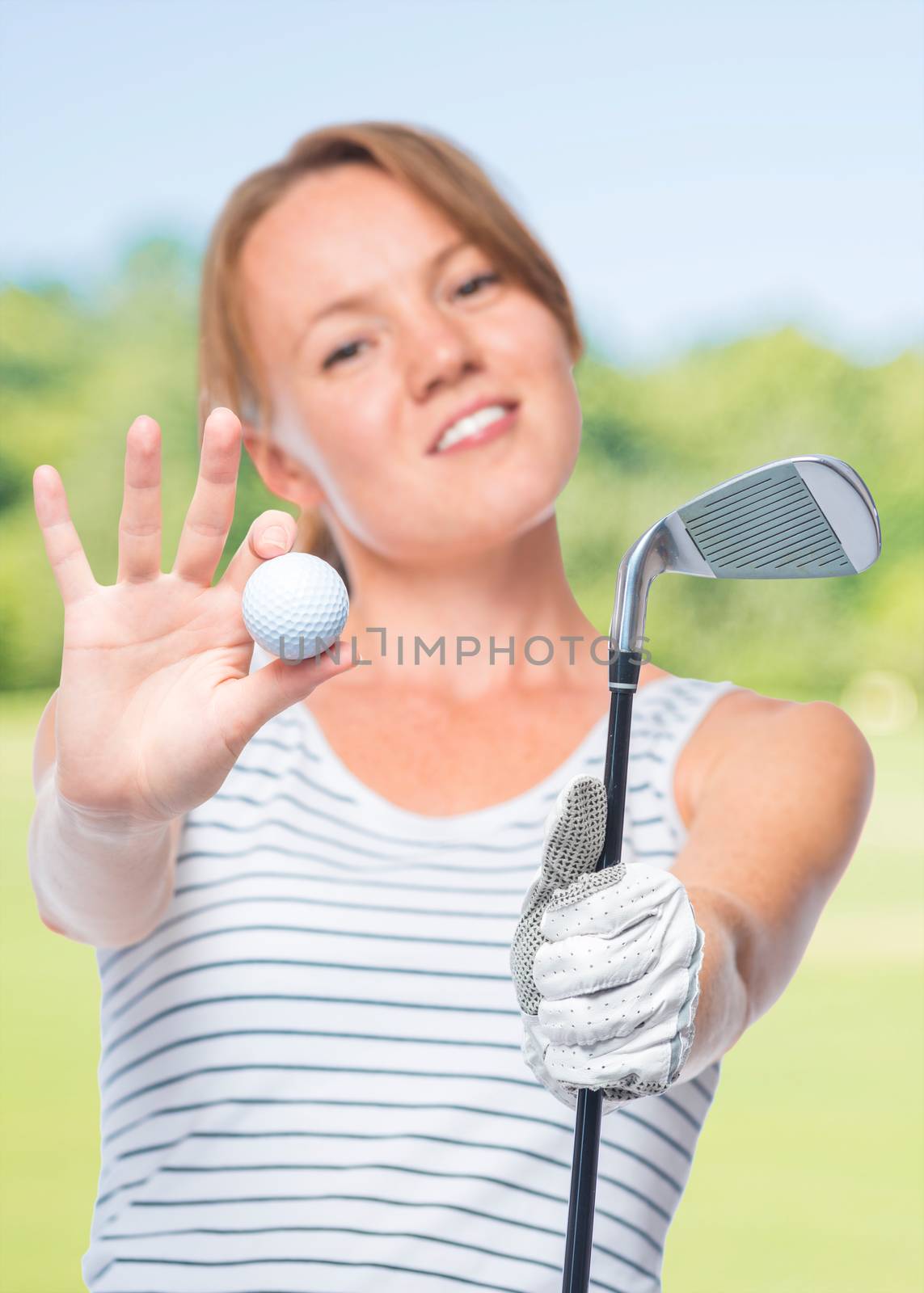 Focus on the ball and a golf club in the hands of a charming girl on a background of golf courses