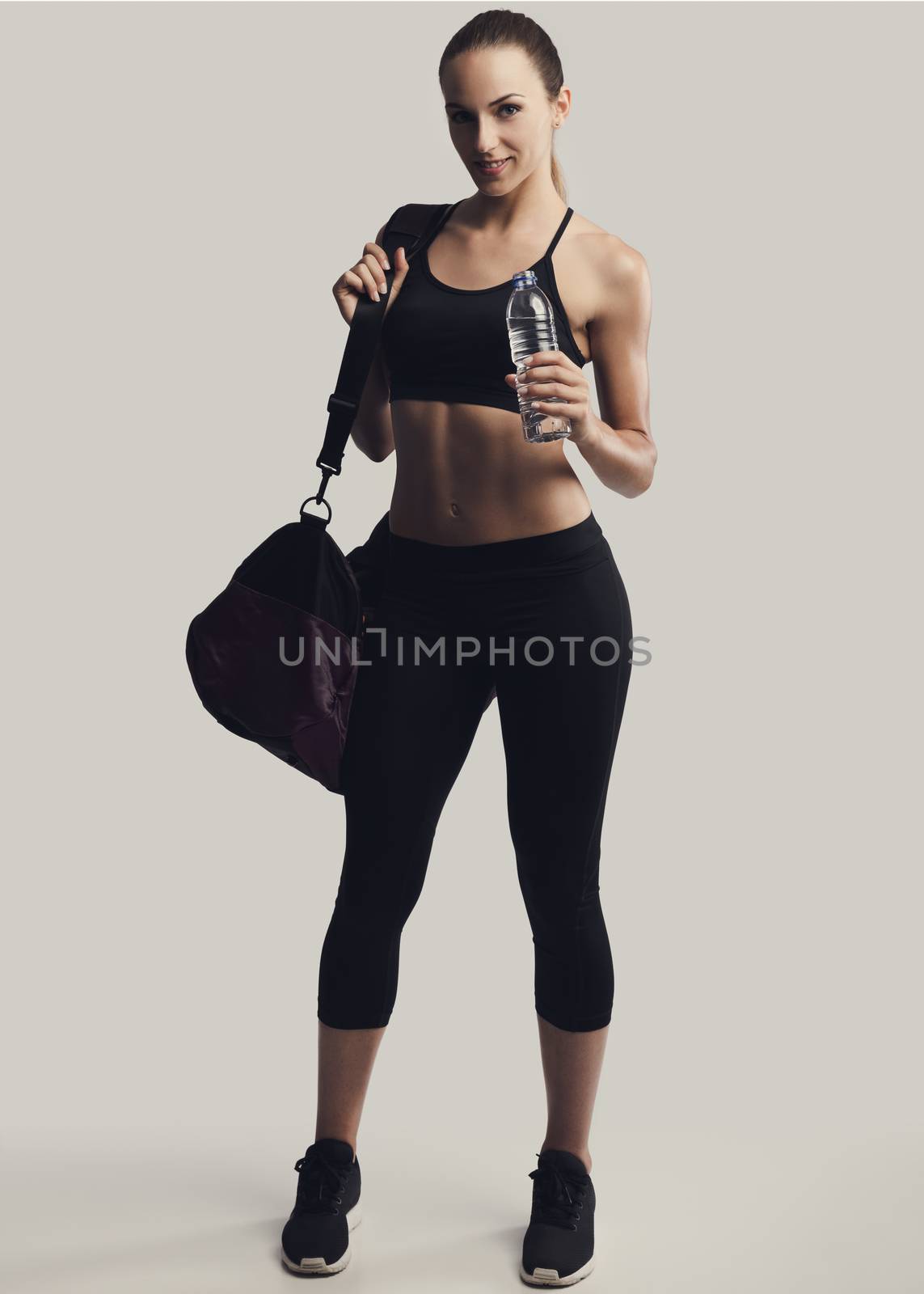 Portrait of sporty young woman posing with a gym bag and holding a water bottle