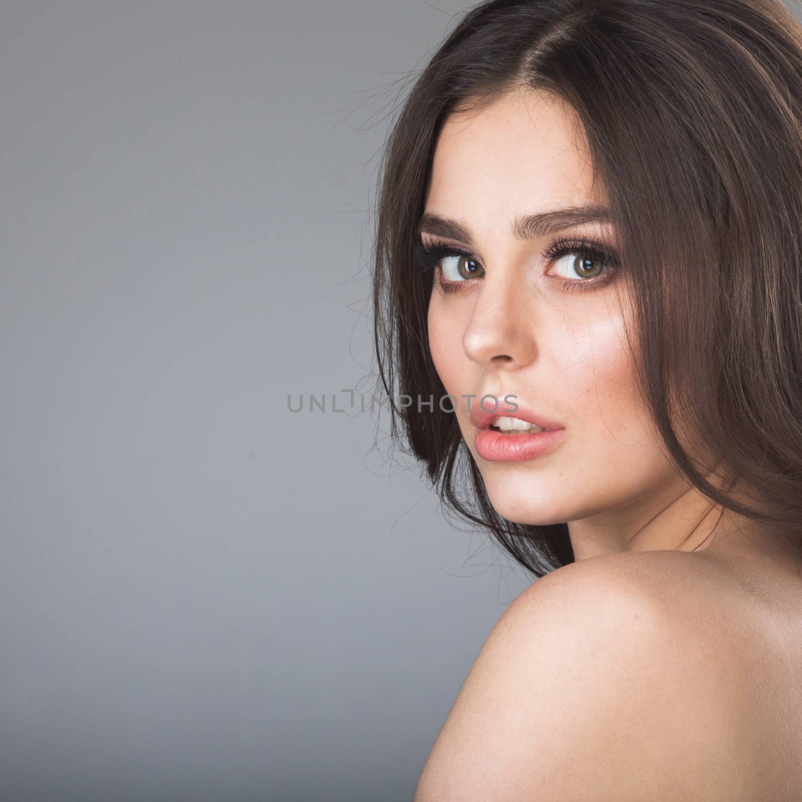 Beauty portrait of young woman with naked shoulder on gray background