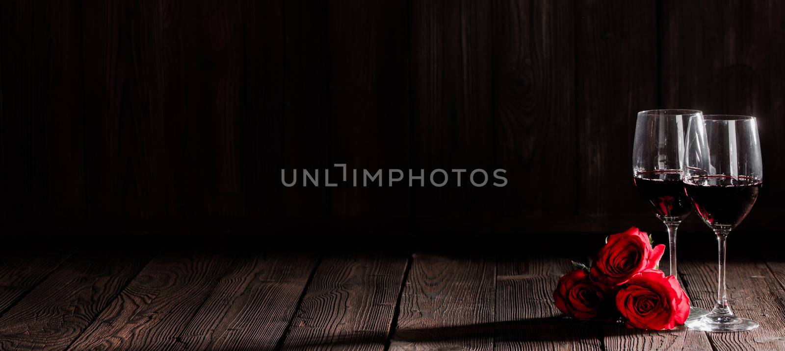 Two glasses of red wine and red roses on dark wooden background, Valentine day