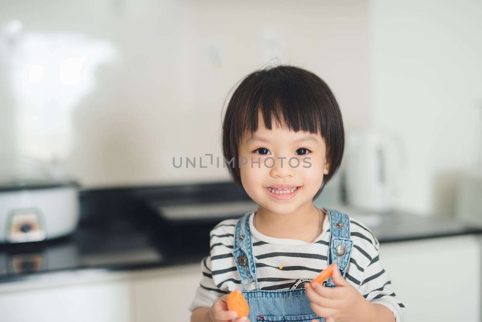 Child girl having fun with carrot. Home kitchen interior with fruits and vegetables.