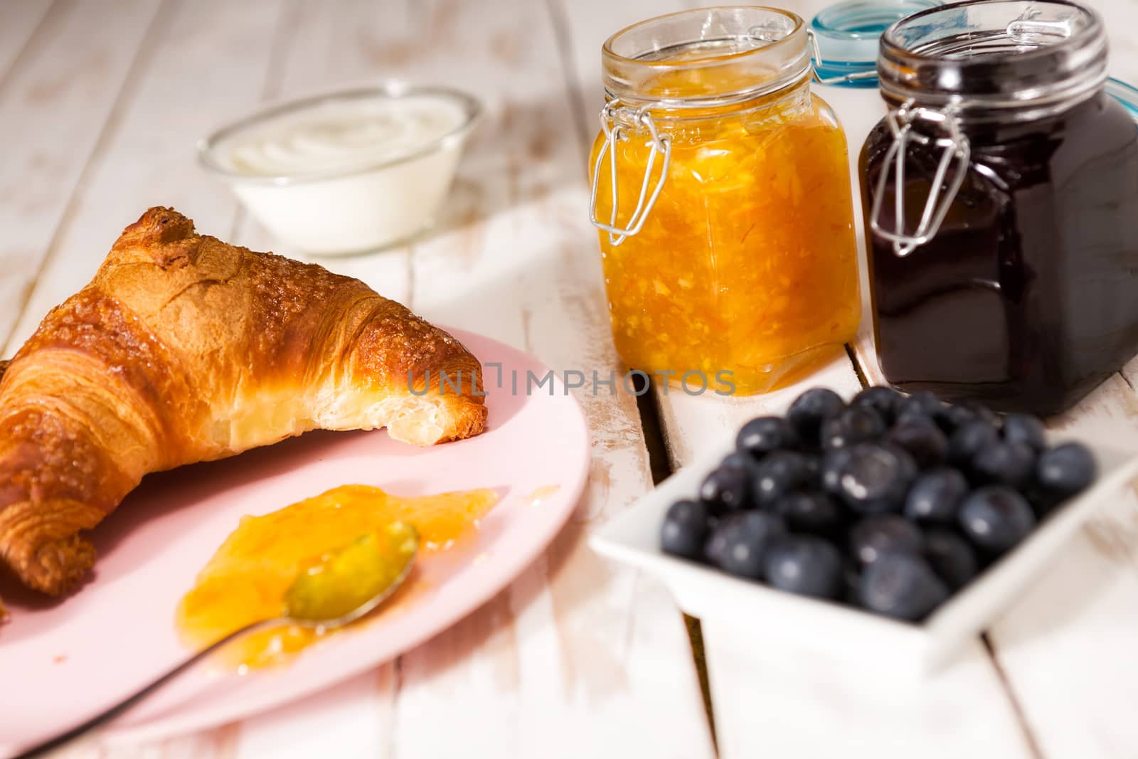 Breakfast with croissant, blueberries, yogurt, orange and blueberry jam over a wooden table