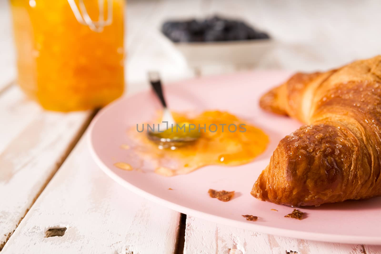 Closeup of croissant and orange jam on a pink plate over a wooden table
