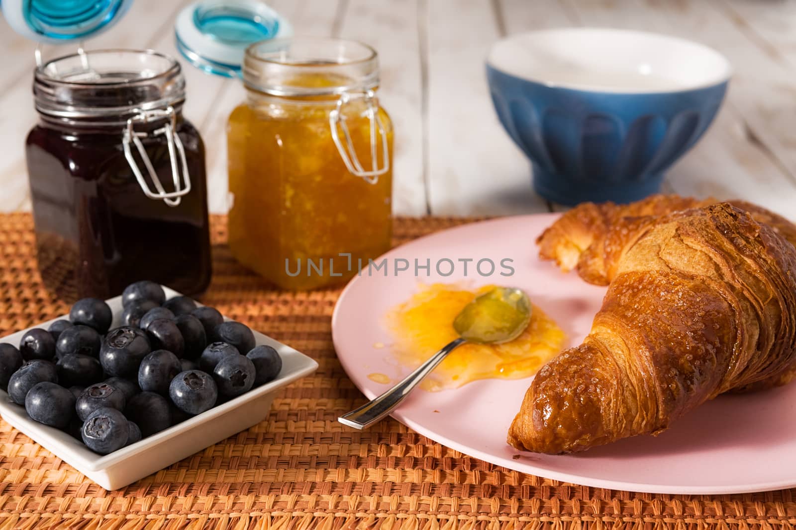 Breakfast with croissant, blueberries, milk, orange and blueberry jam over a tablecloth
