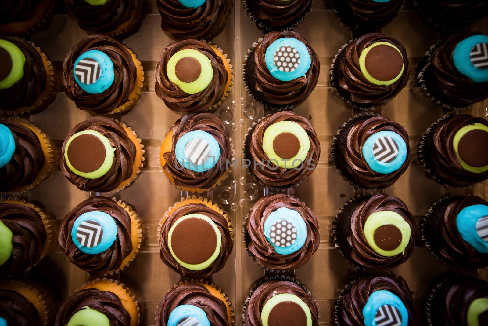 A wide top down shot of colorful icing covered covered cupcakes all put in a row.