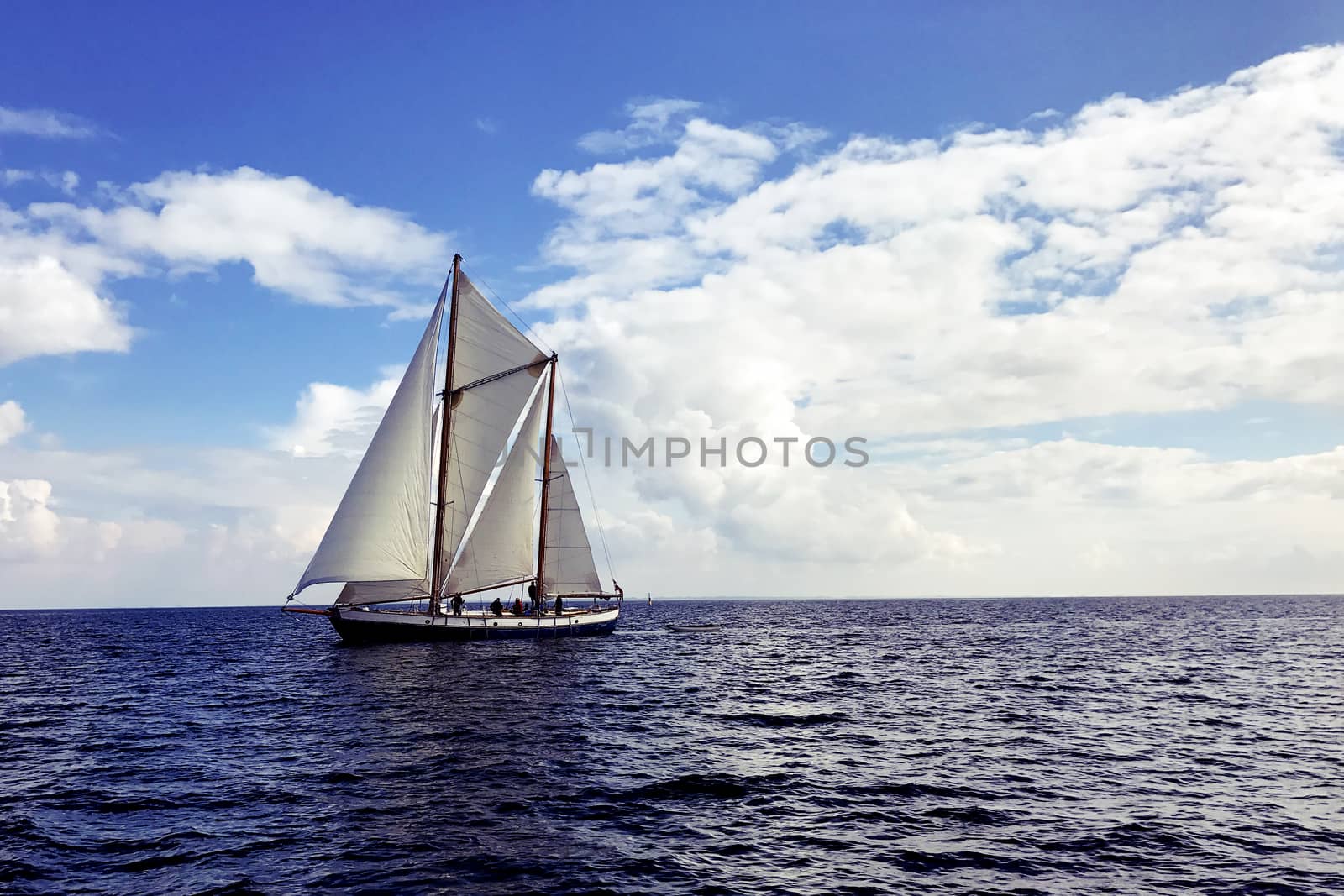 Vintage sail boat sailing on dark blue ocean under blue and cloudy sky.