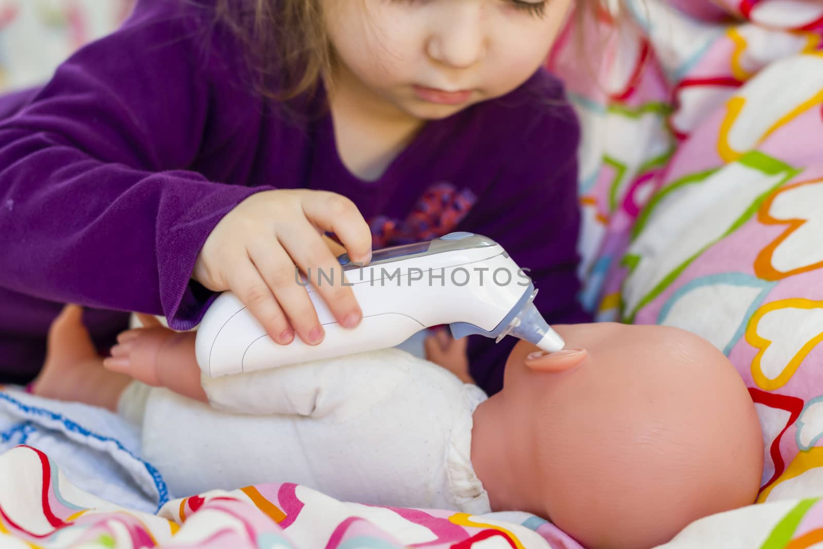 Little girl playing doctor with a doll, measuring temperature wi by asafaric