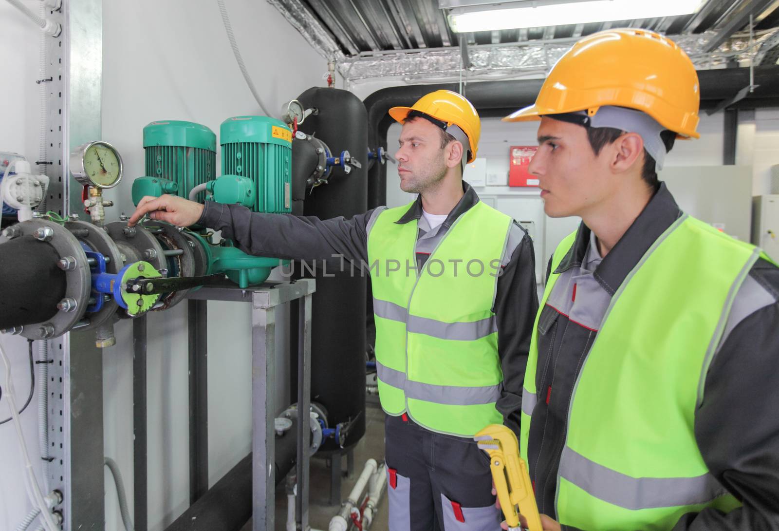 Two workers in hardhats at plant checking parameters of pressure