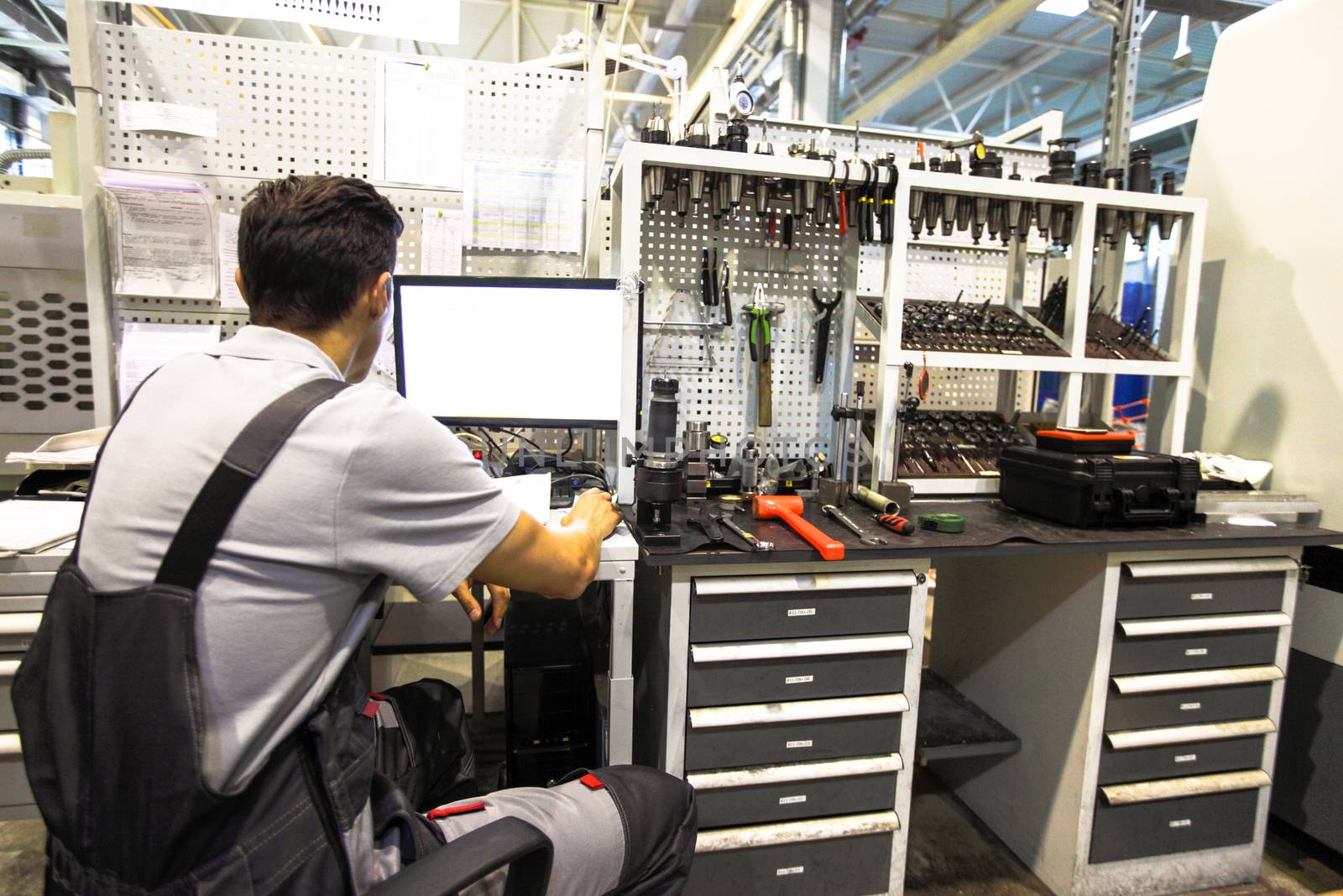 Worker at workplace with computer and tools at CNC factory