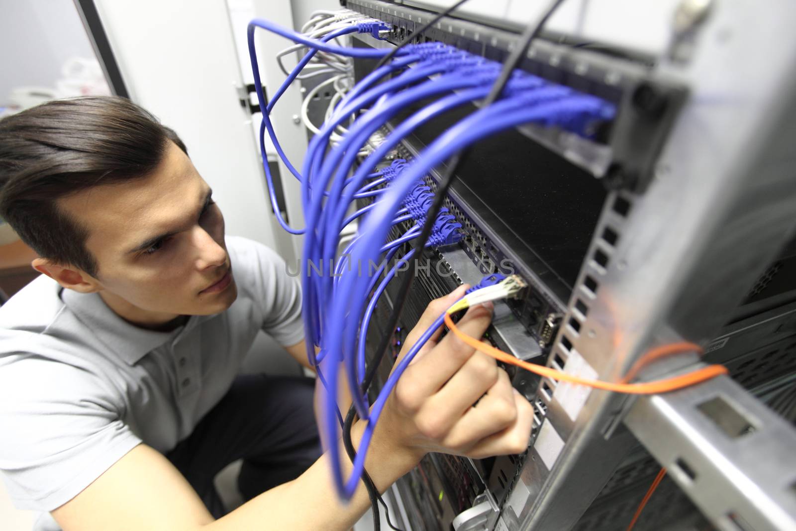 Young engeneer man in network server room connecting wires and checking rack devices