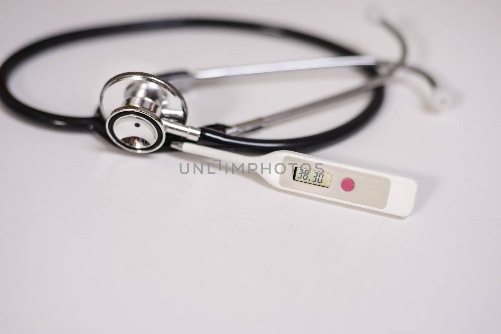 A thermometer showing high body temperature and stethoscope in background on white surface