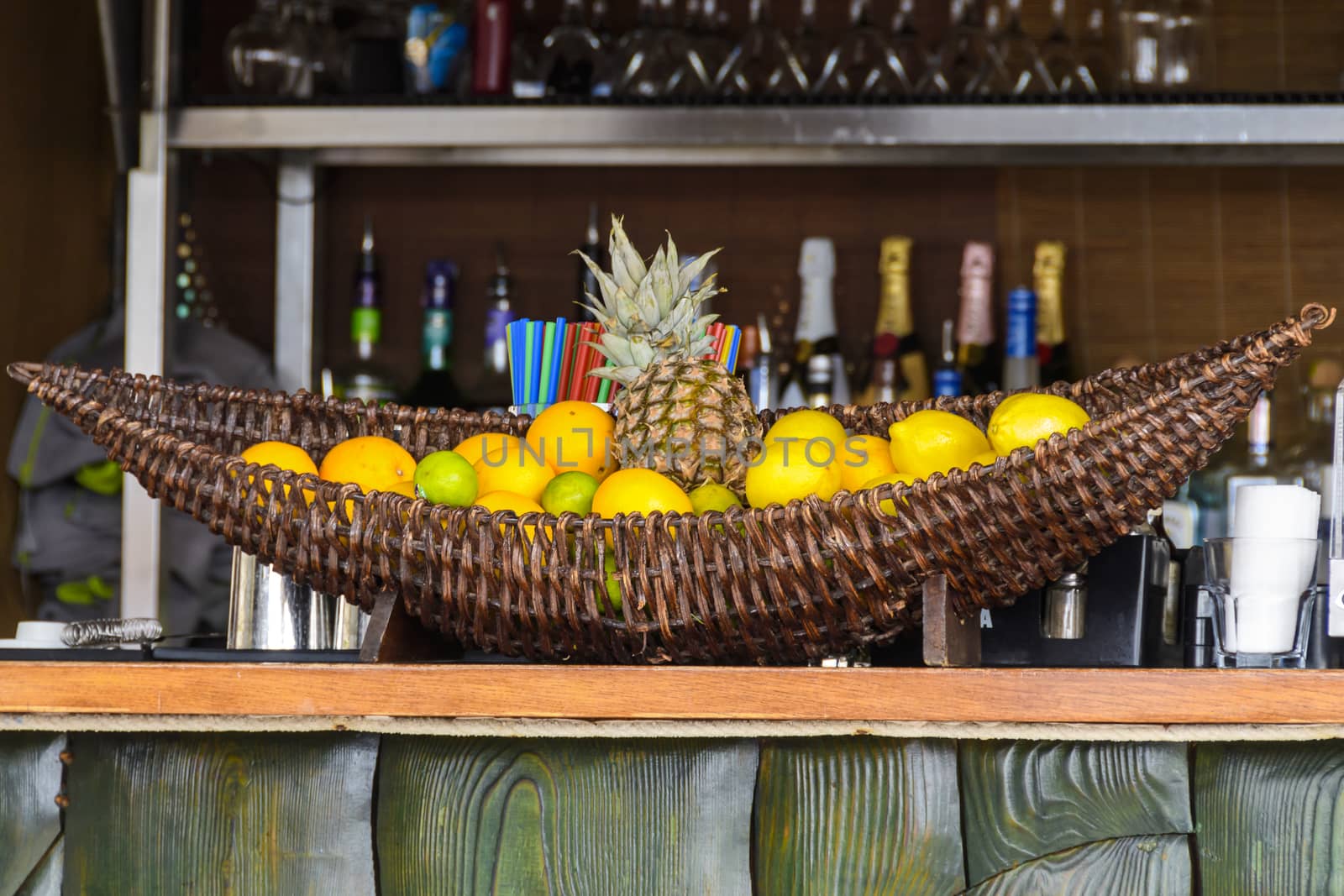 Bar counter with fruits in basket and shelfs with bottles in background