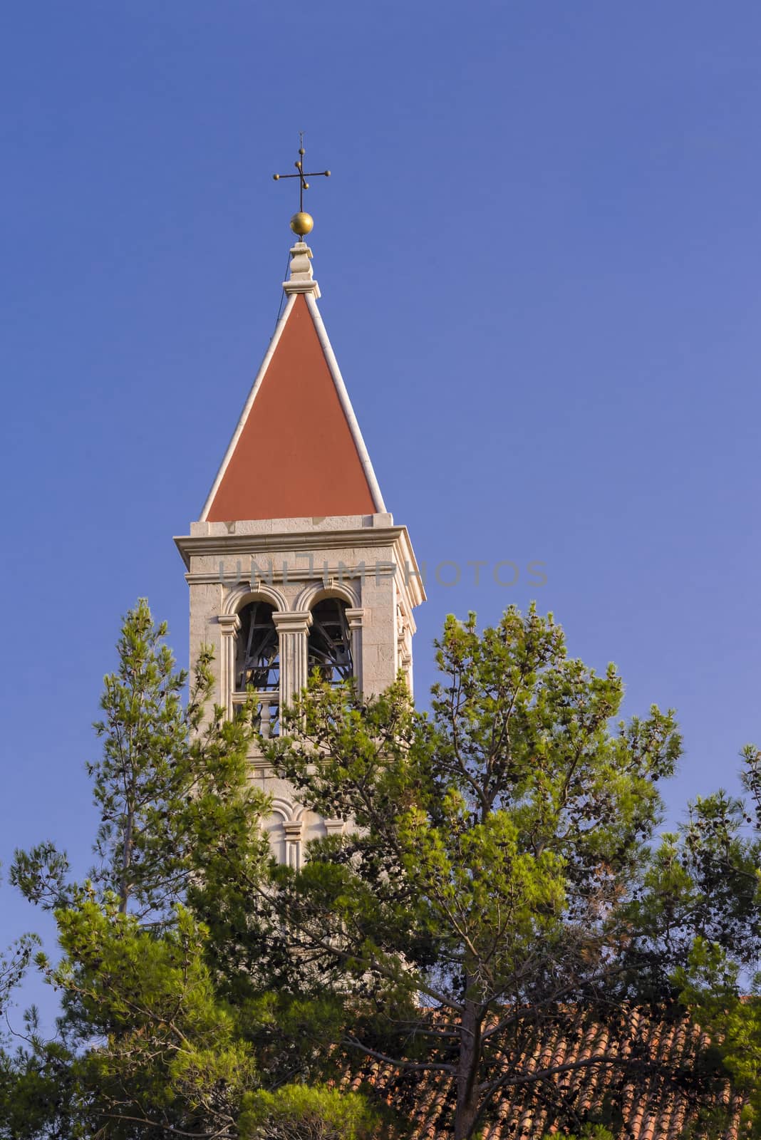 Christian church steeple in front of pines on blue sky with red roof and cross on top