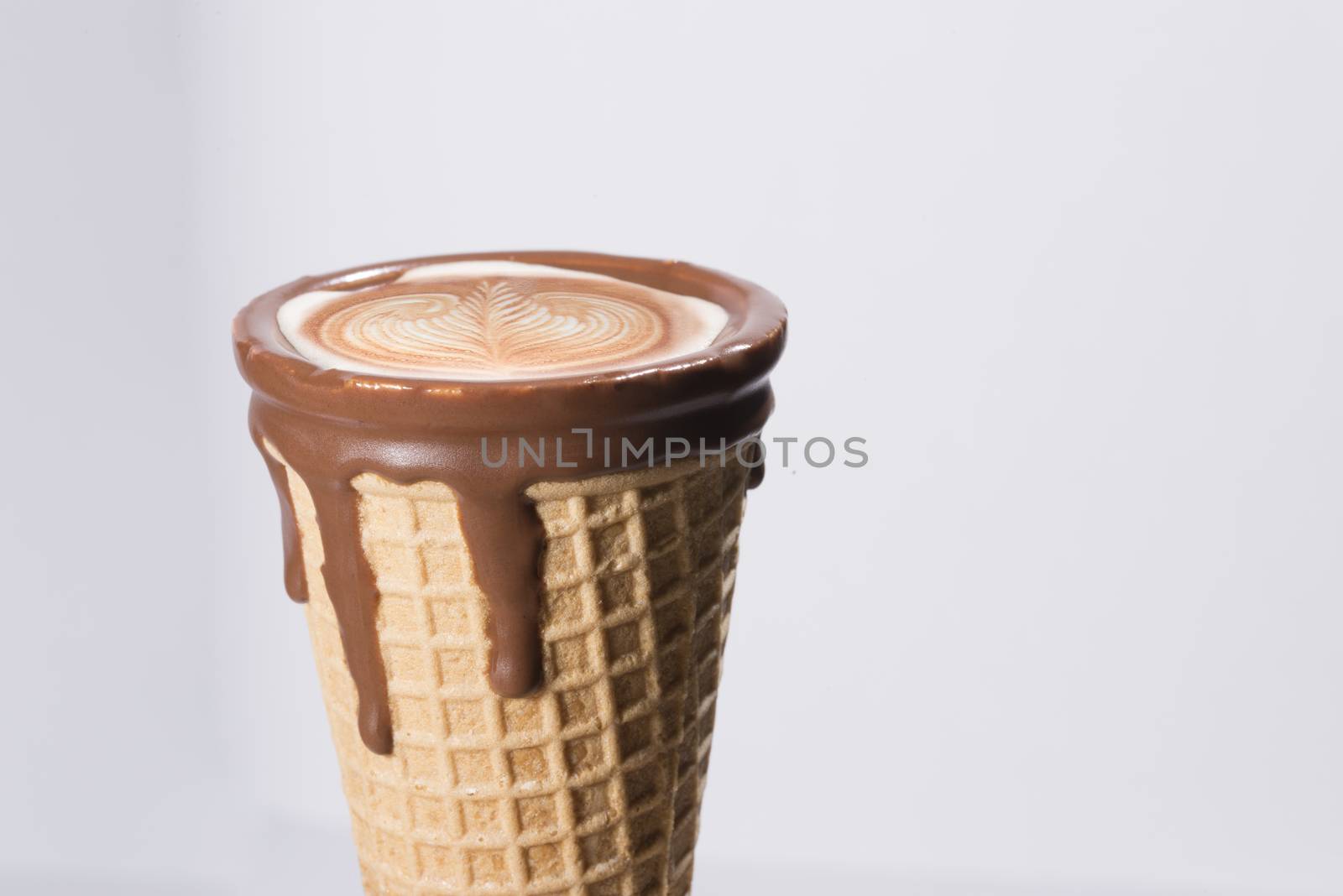 Coffee in waffle cone dipped in chocolate with drawings in capuccino / latte milk foam, latte art, isolated