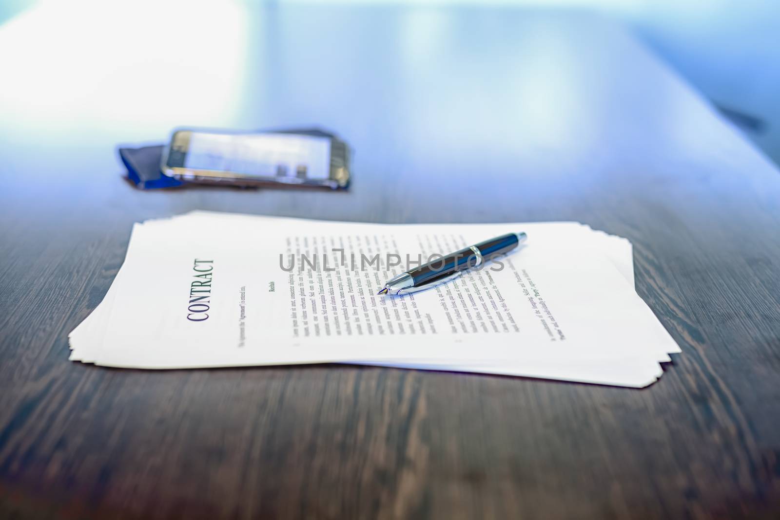 Business contract / agreement and fountain pen on dark wooden desk, with mobile phone in background, shallow depth of field, low angle