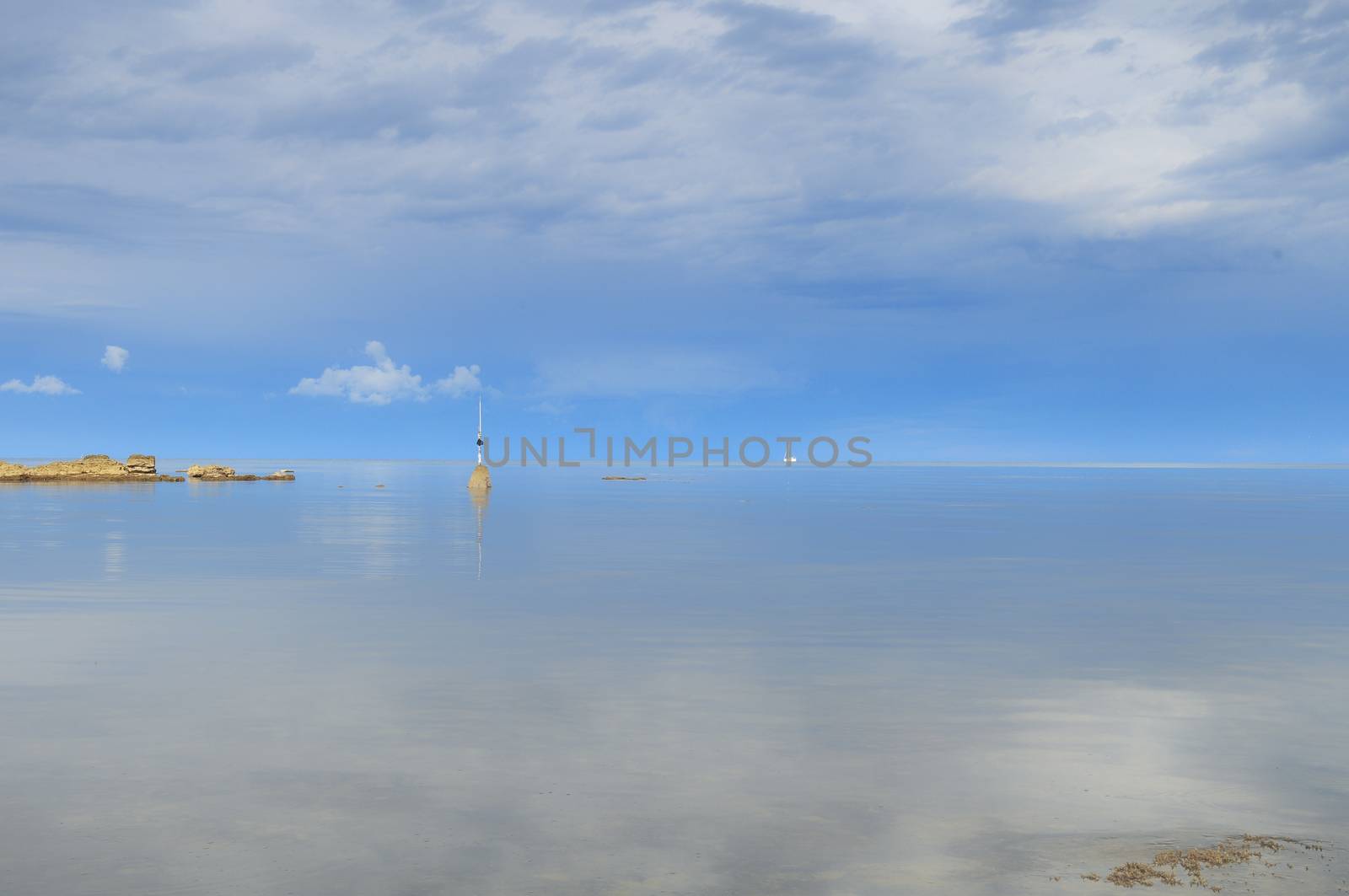 Morning at the seashore with misty water and diffuse light cased an almost surreal lighting situation. Blue skies, silky water and a sailboat complete the picture. Croatia, Istria