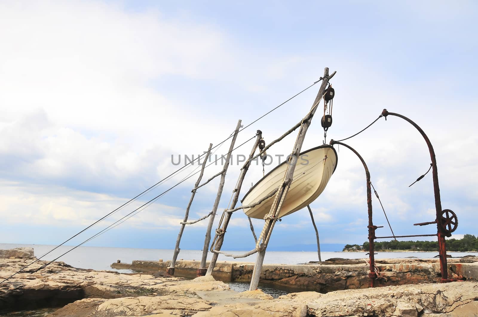 Small fishing boat hoisted on traditional crane by asafaric