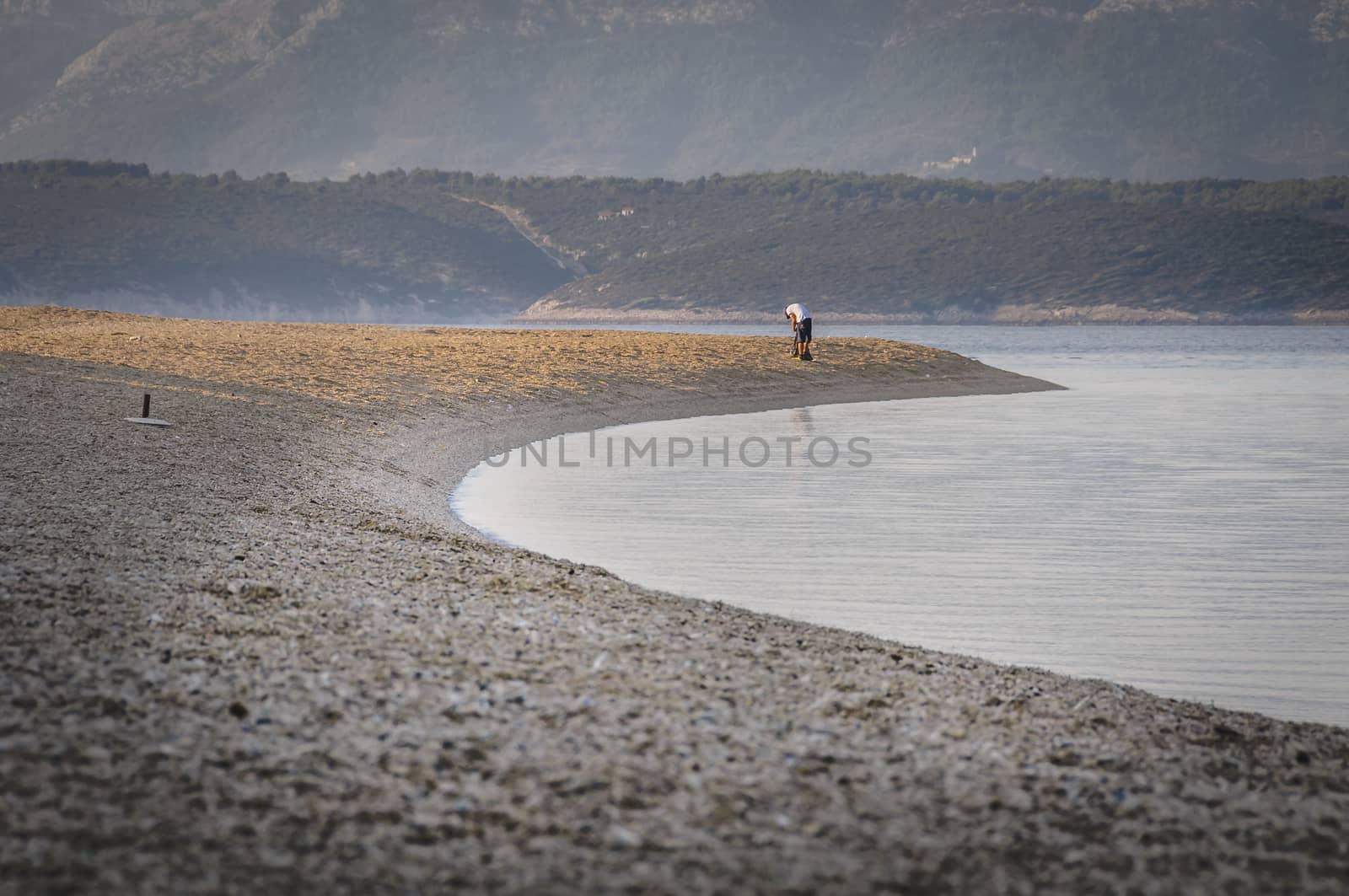 A lone man, facing away from the viewer, early in the morning cleaning the beach before tourist arrive