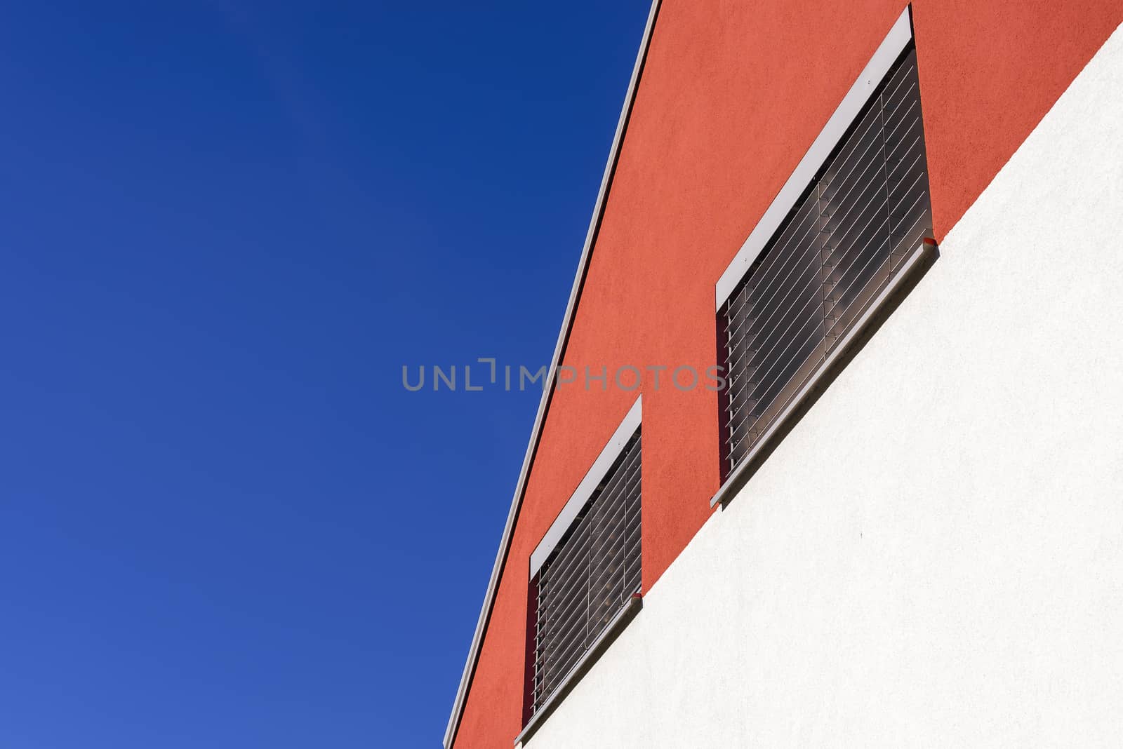 Colourful graphic architectural design; orange and white facade with silver alluminium venetian blinds and blue sky as background