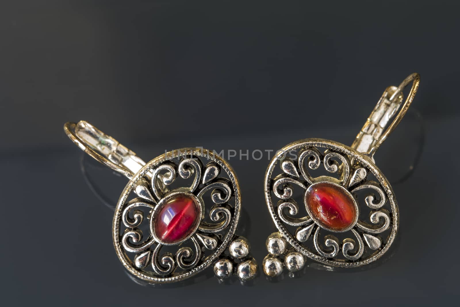 Silver earrings with red gems on dark background with beautiful reflection, close up macro shot