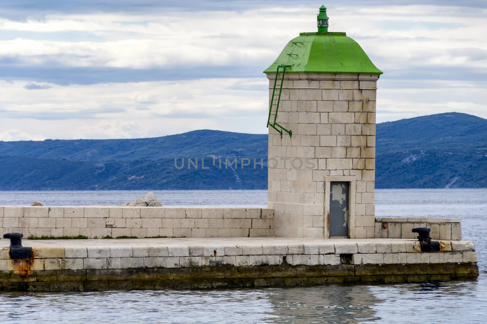 Stone lighthouse in harbour with green roof on stone pier by asafaric