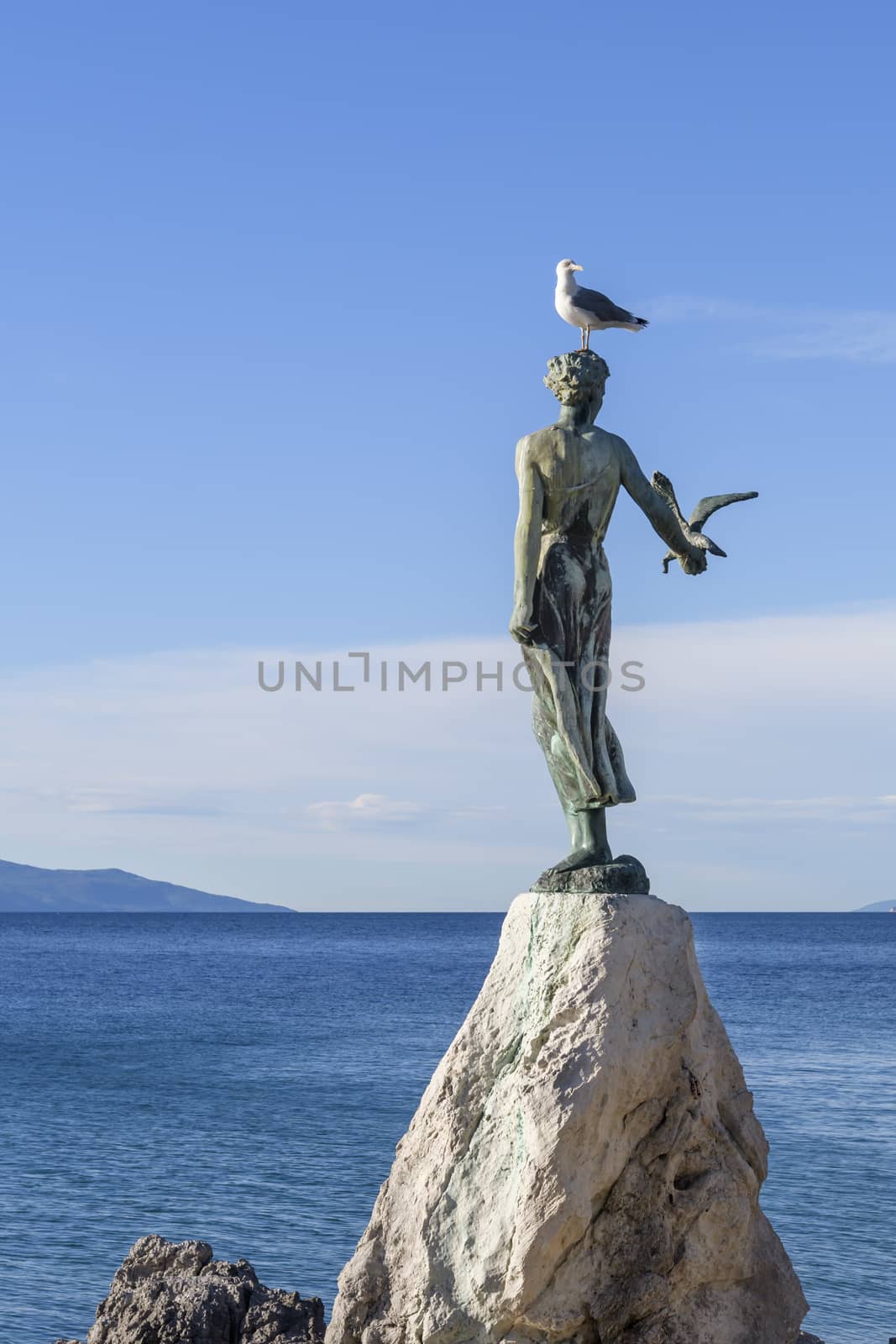 Maiden girl holding a seagull and facing the sea, statue on rocks, Opatija, Croatia