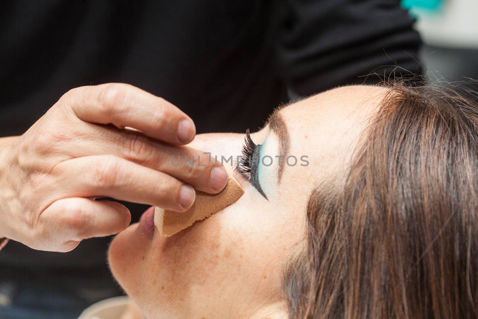 Makeup artist applying foundation using a sponge to a white woman