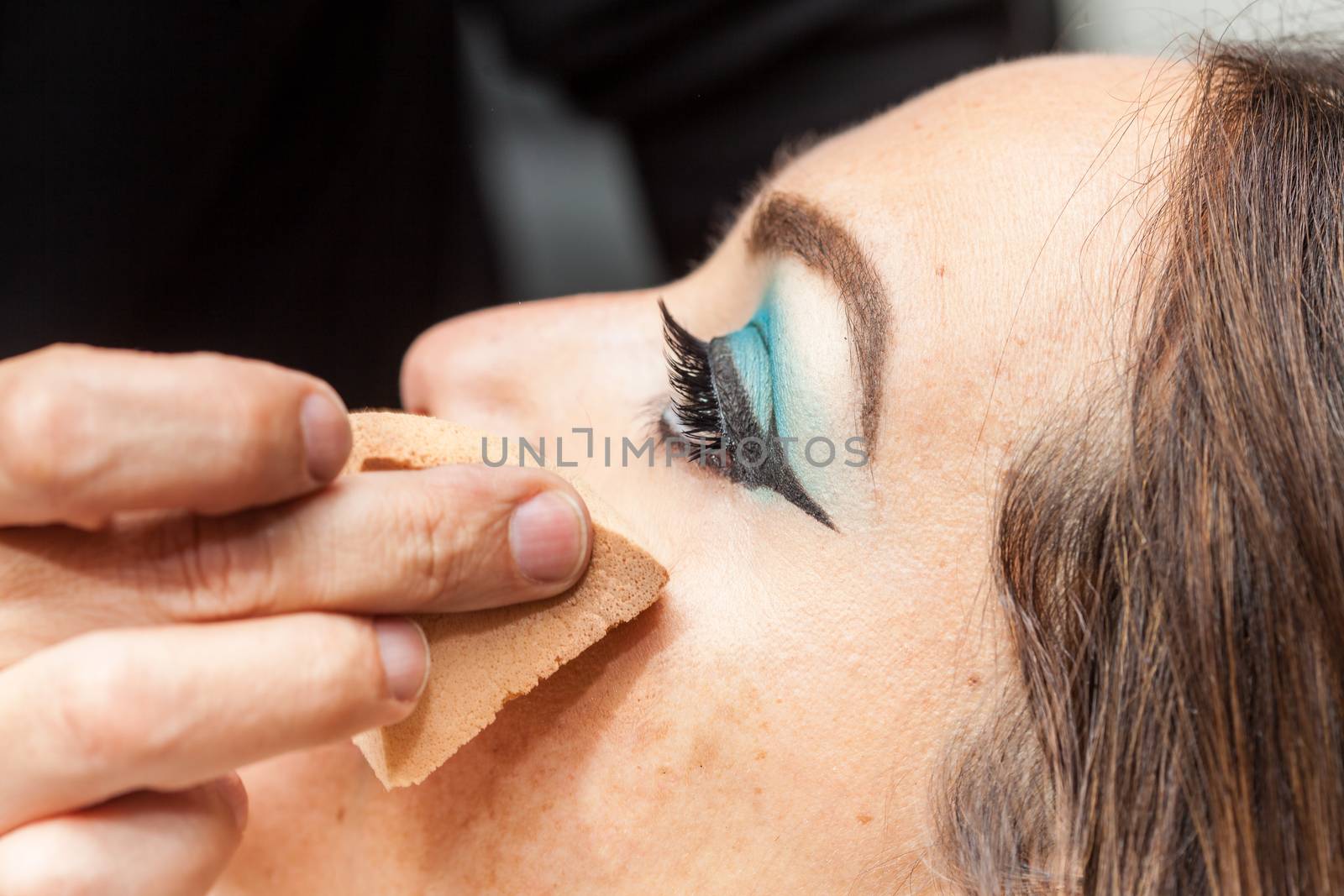 Makeup artist applying foundation using a sponge to a white woman