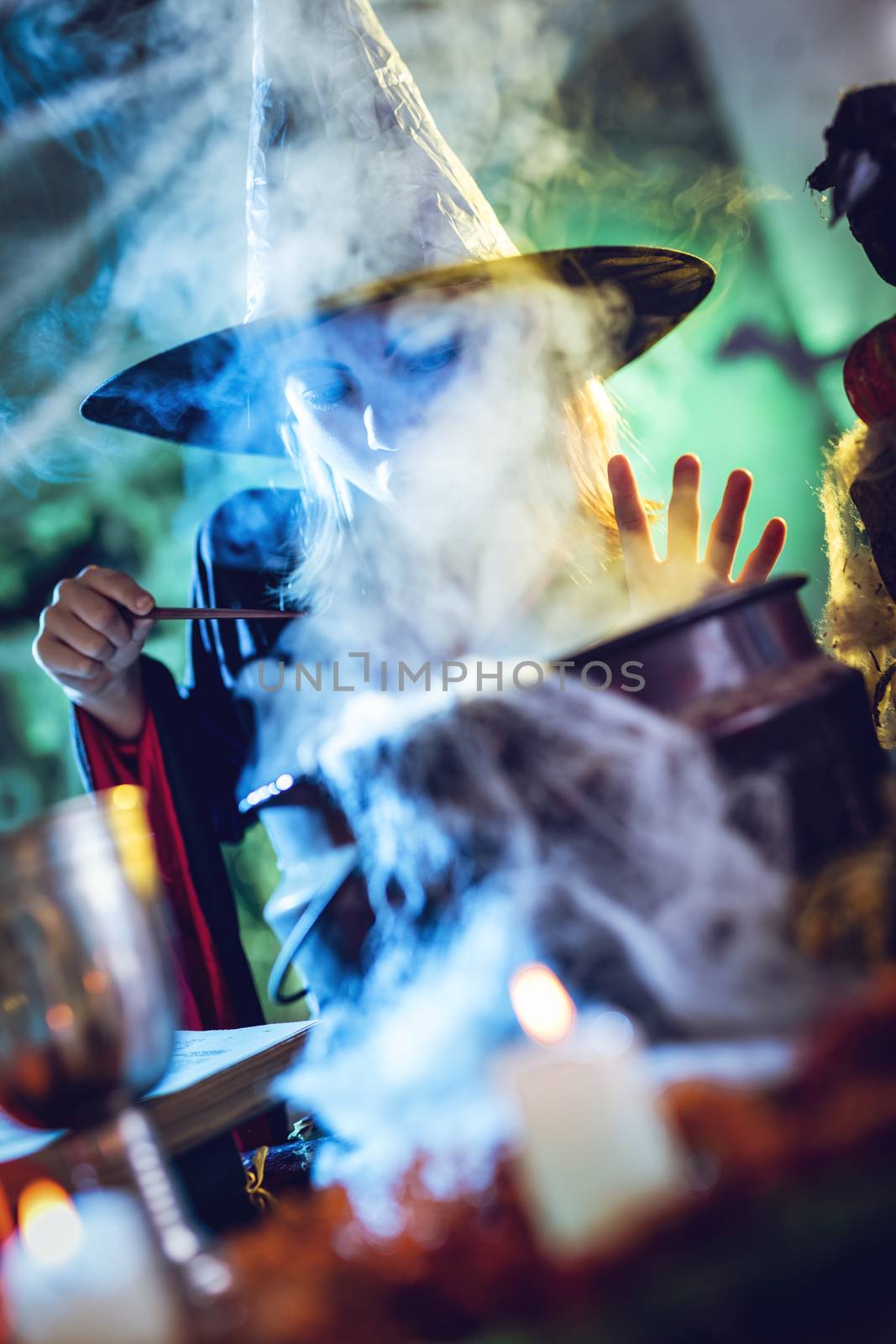 Young witch with face is hidden in steam and fog, sends magic to magic potion in cauldron in front her.