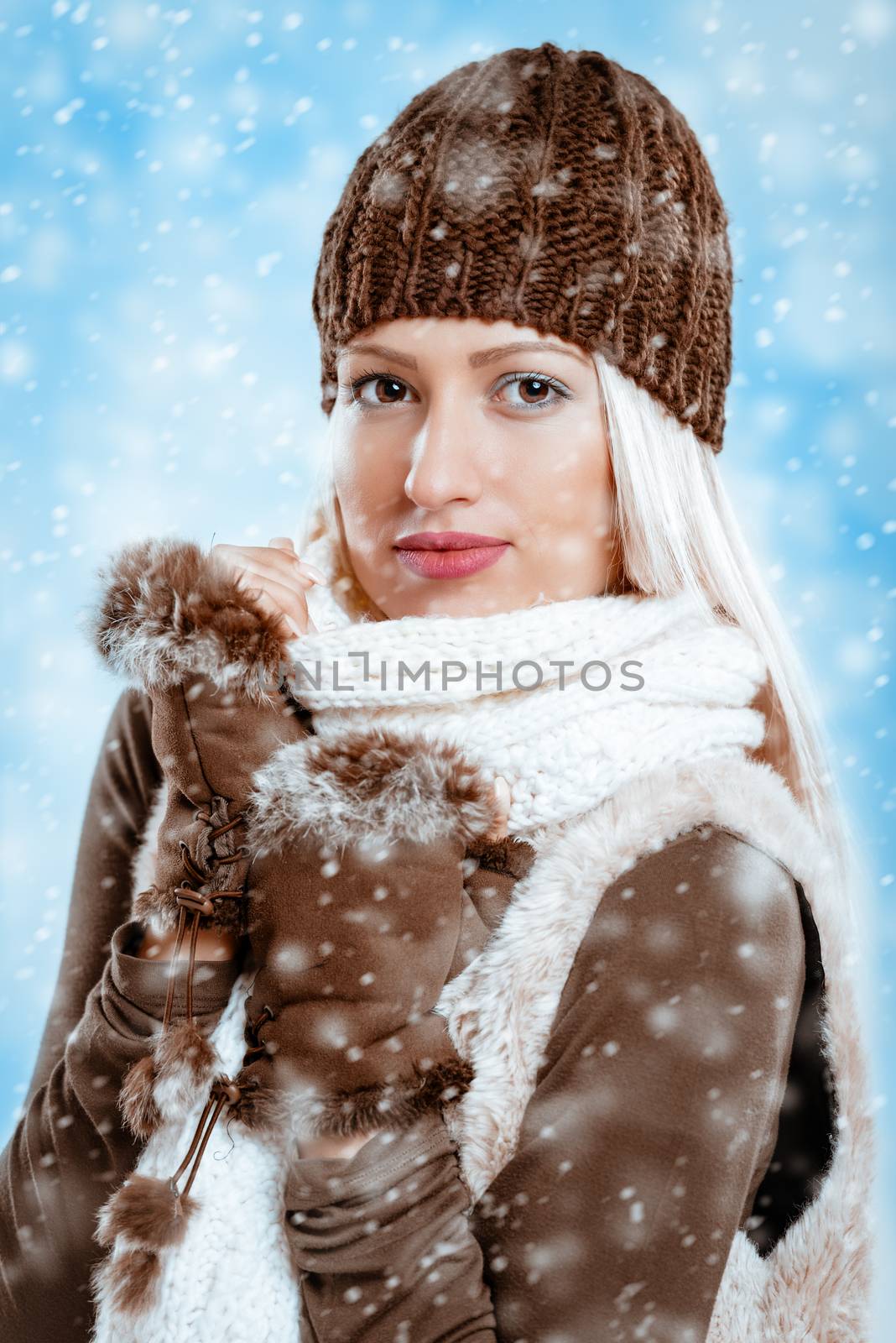 Beautiful young girl in winter clothes with a wool cap and fur gloves, sticks to the wool scarf in which is tucking while snow falling.