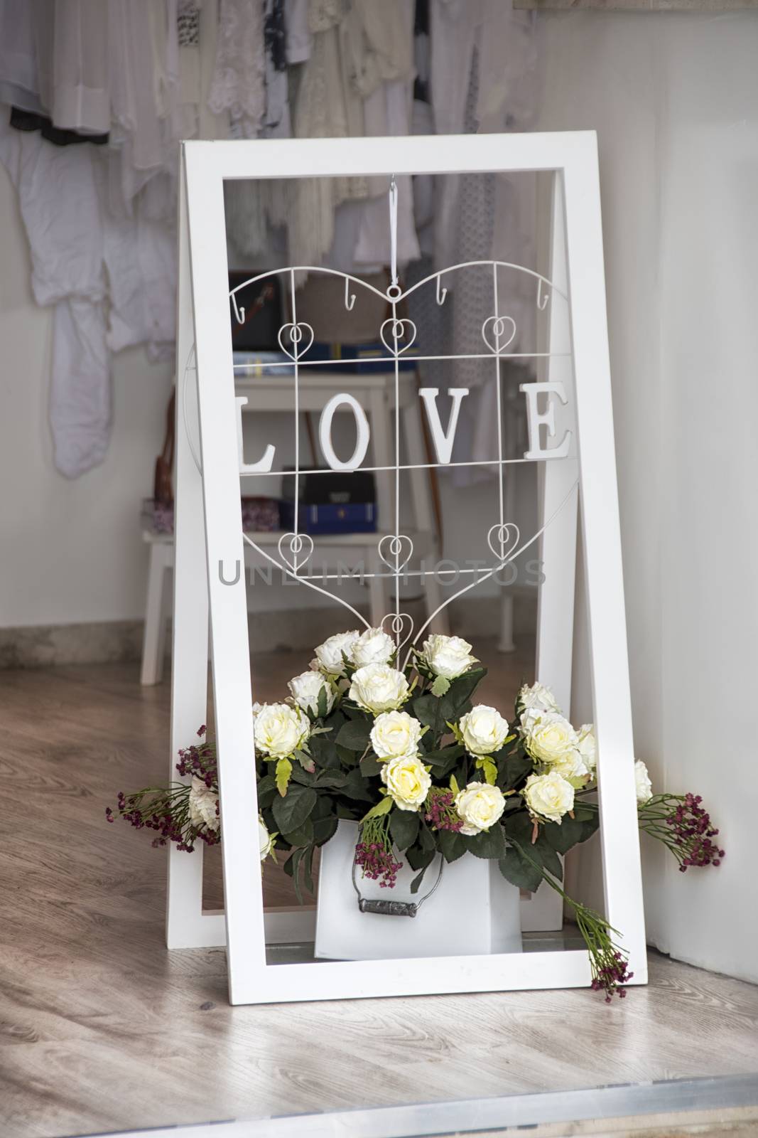 A white frame with LOVE inscription and white roses as decoration of apparel shop, boutique entrance
