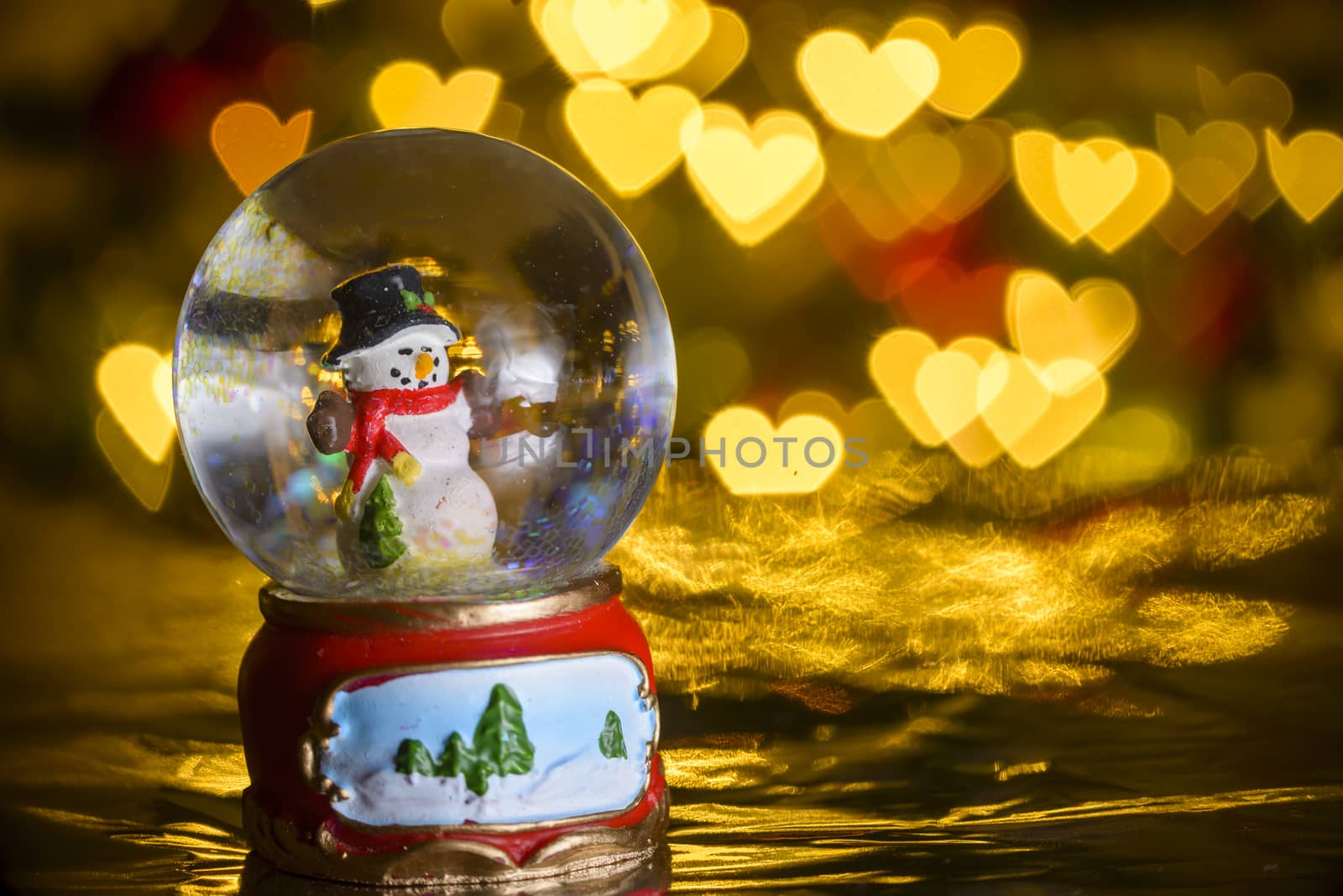 Christmas snow globe with xmas lights in background; snowman with presents; heart shapes, bokeh blur