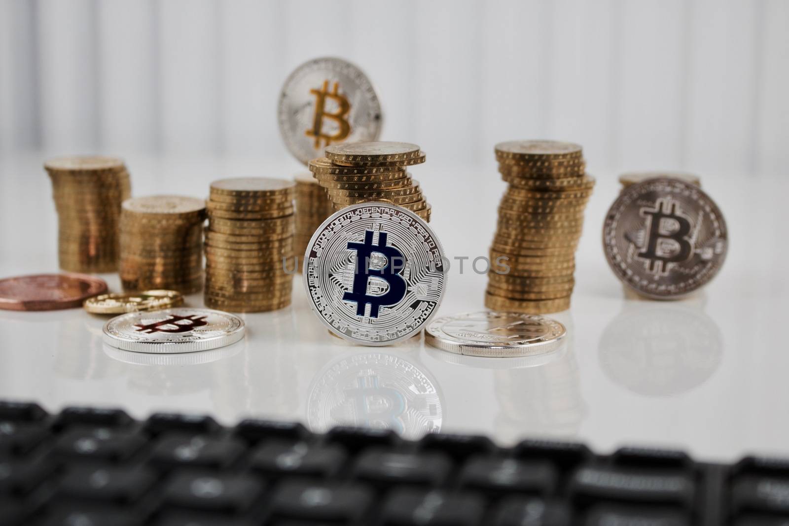 Digital currency physical silver bitcoin coin on the table near gold money and computer keyboard.