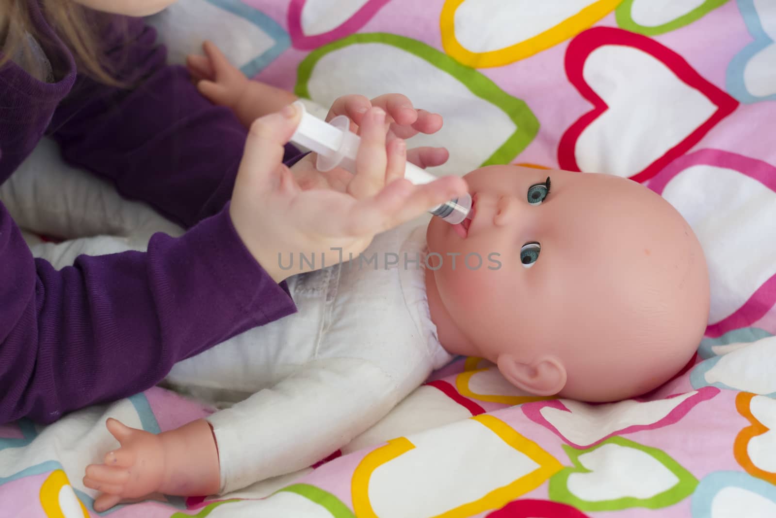 Little girl playing doctor with a doll and applying medicines with syringe and taking care of a doll, concept maternity, lifestyle and childhood