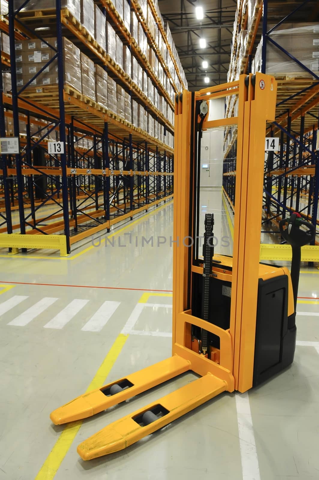 Yellow forklift in front, in back view through the racks of a large warehouse