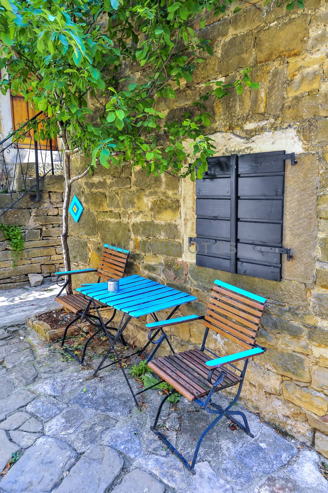 A pair of turquise chairs and a table in an idylic instrian village in the shade of an old stone house