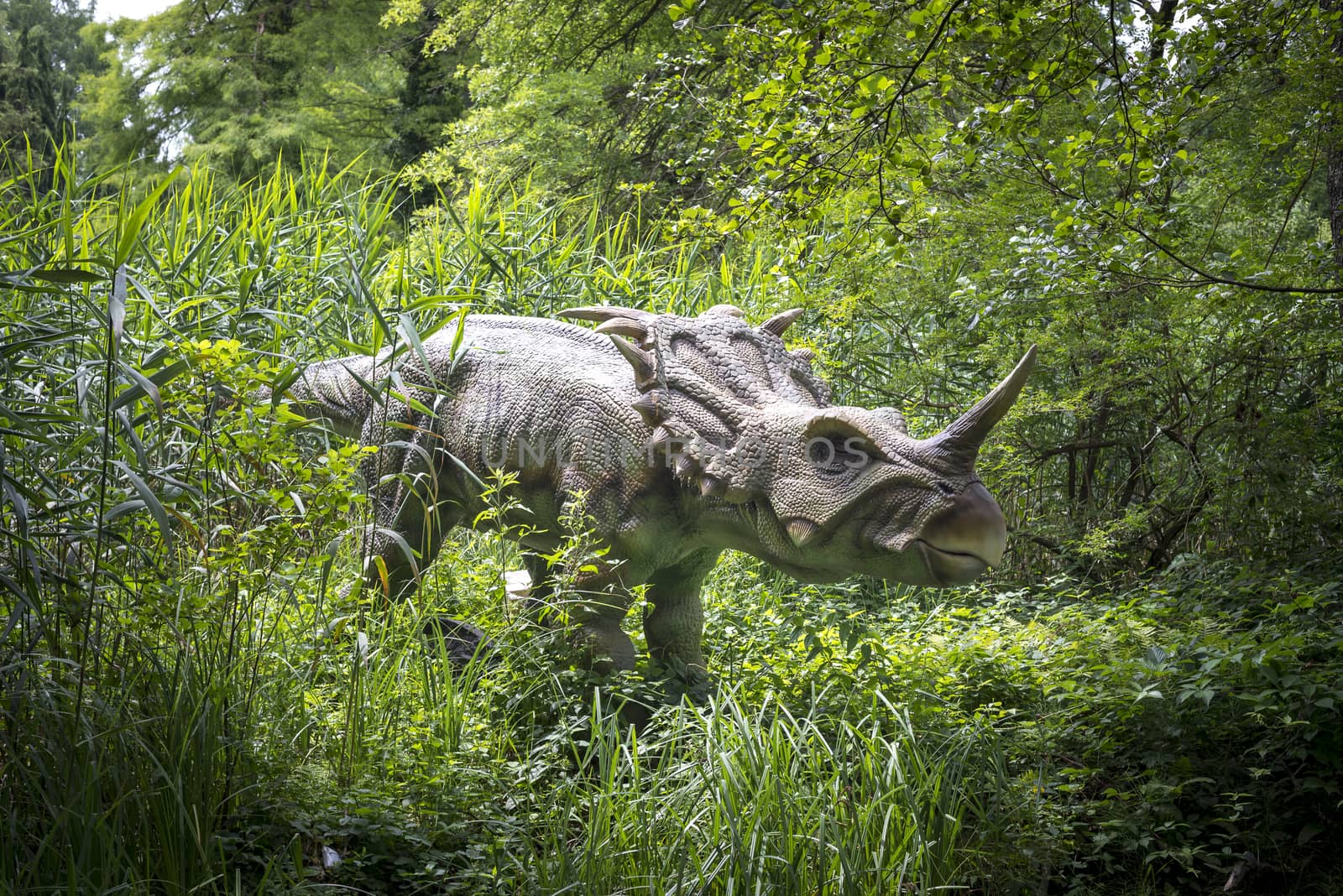 A dinosaur statue in a recreation park, greenery in background