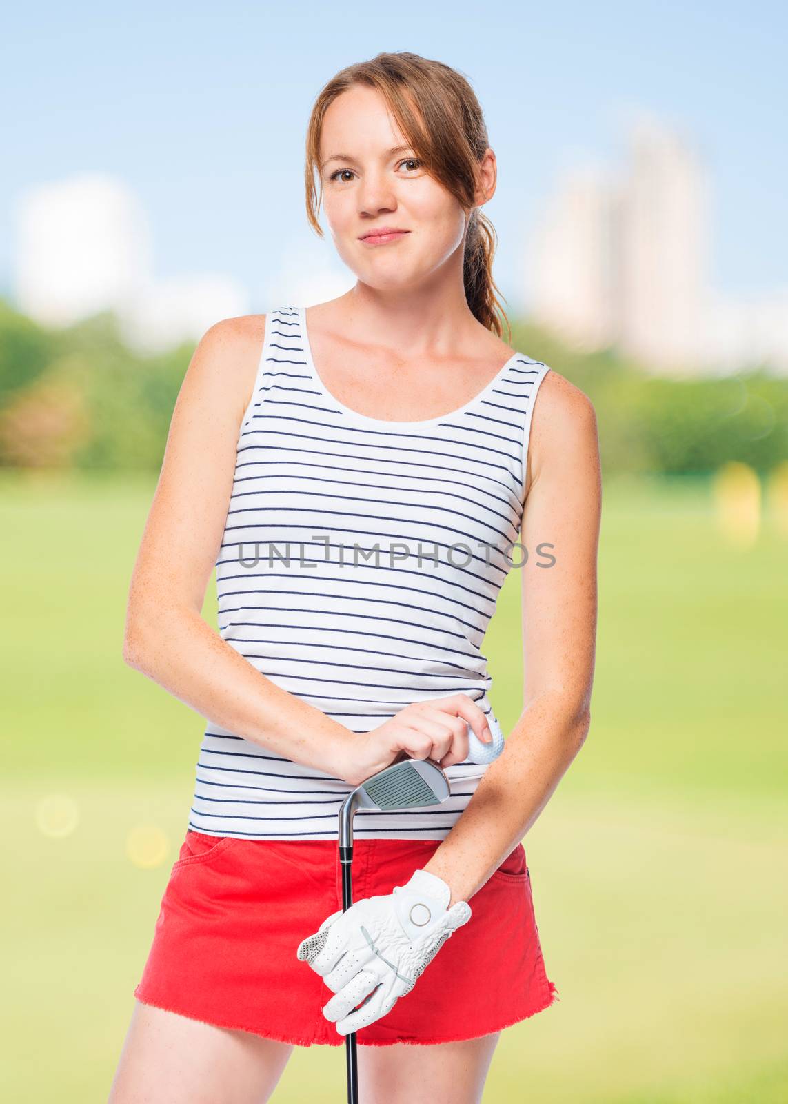 Girl in a striped T-shirt posing with a golf club on a background of golf courses