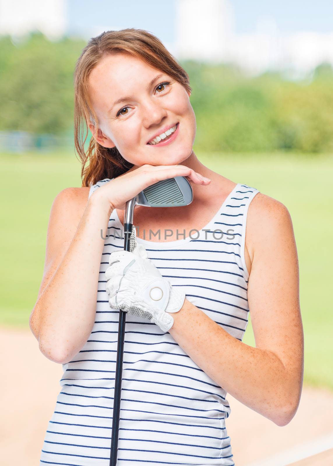 Cute girl with a golf club on a background of golf courses in a striped T-shirt