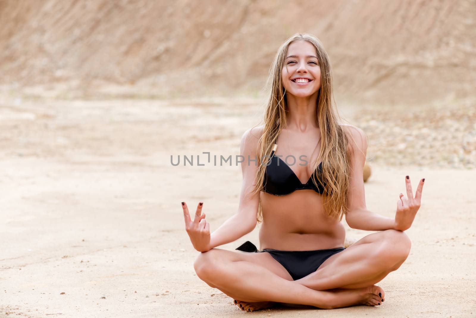 cheerful slender woman in lotus position on the beach