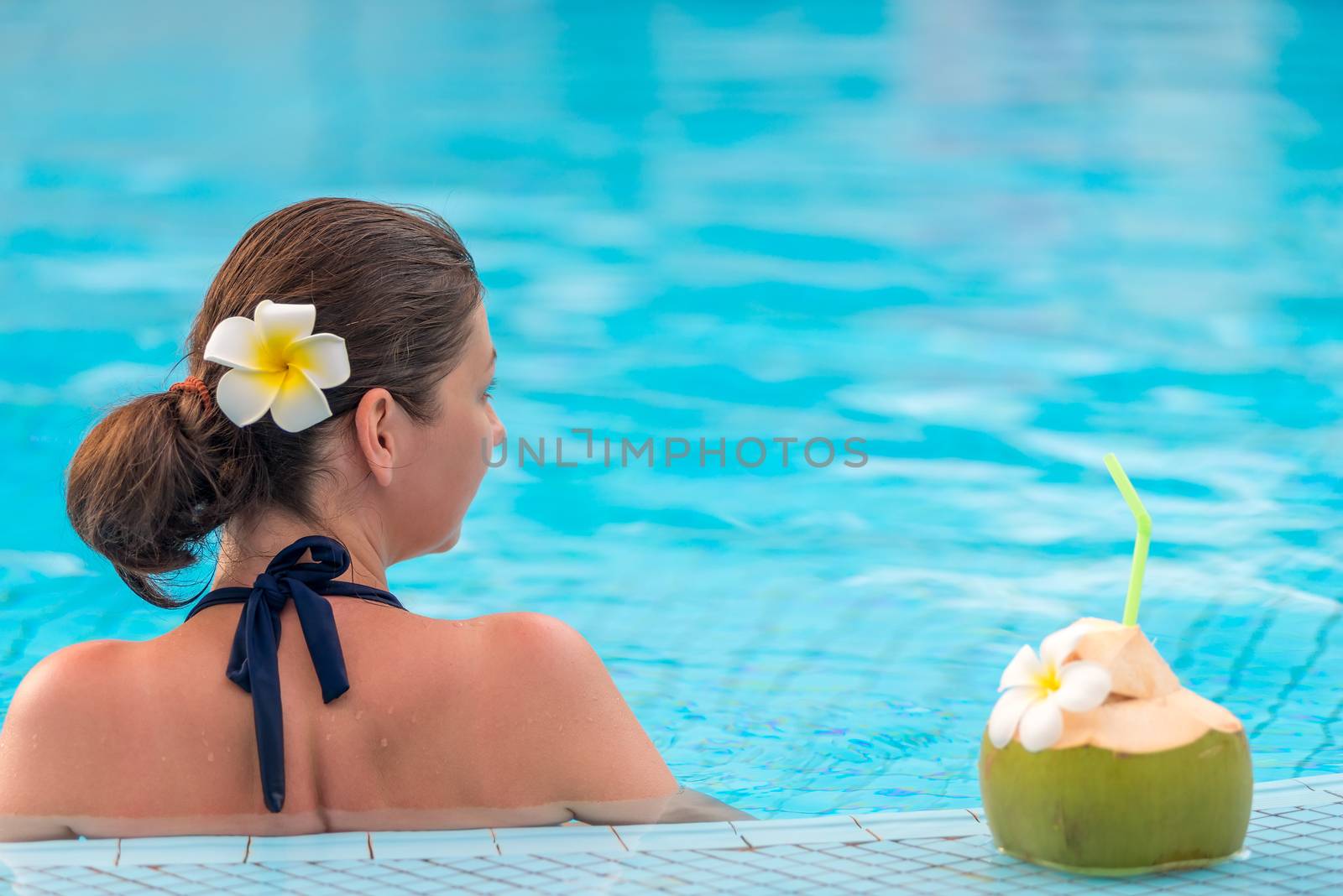 brunette relaxes in the pool, standing near a coconut with a straw