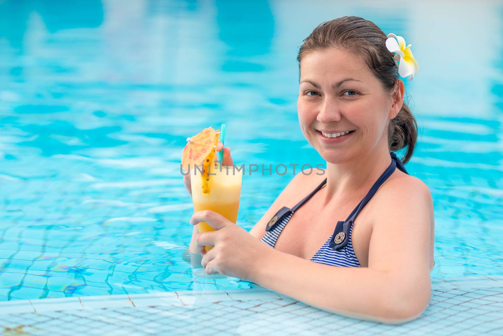 woman with a flower in her hair drinks a delicious cocktail in the pool