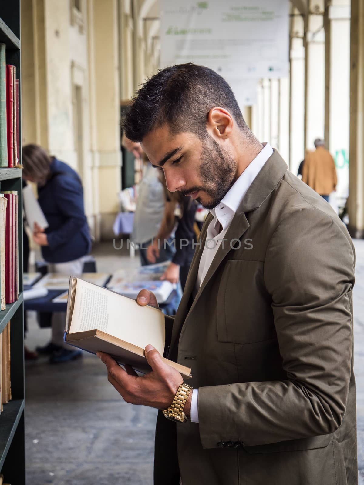 Side view of handsome man in elegant suit reading book in library.