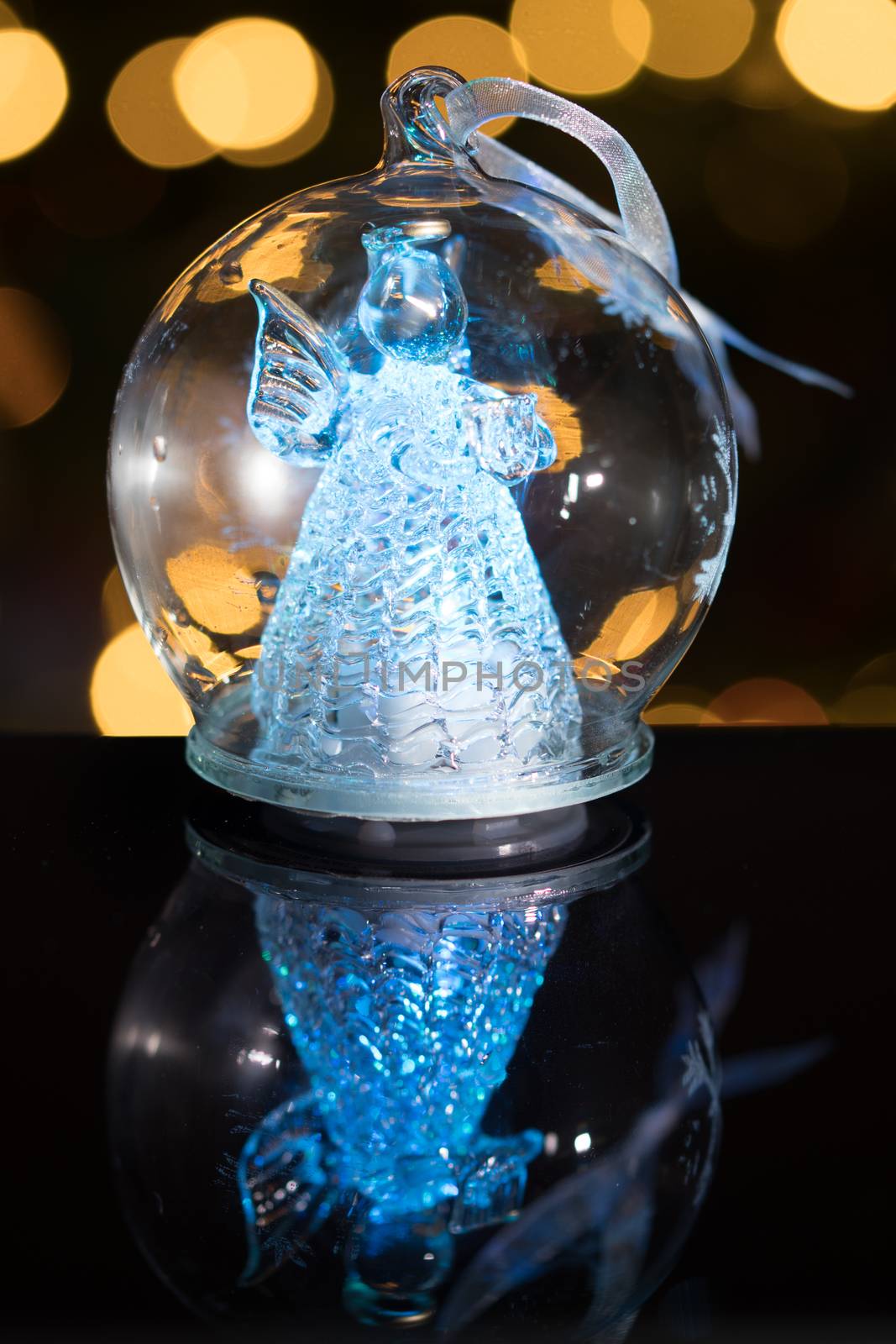 Illuminated angel figure in glass bulb, soft boke christmas lights as background, Christmas decoration