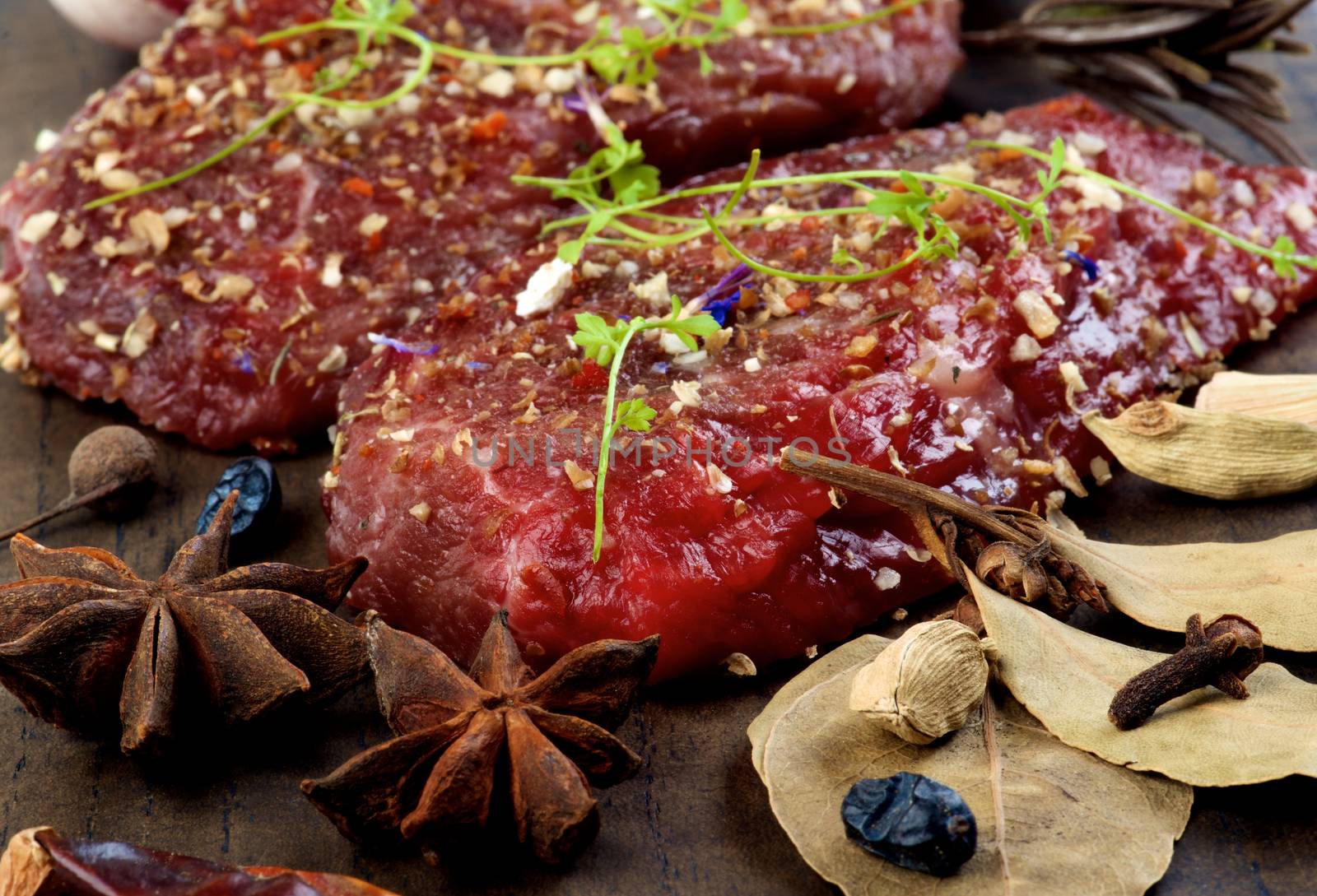 Two Marinated Raw Boneless Beef Steaks with Herbs and Spices, Garlic and Chili Pepper closeup on Wooden Cutting Board. Focus on Foreground