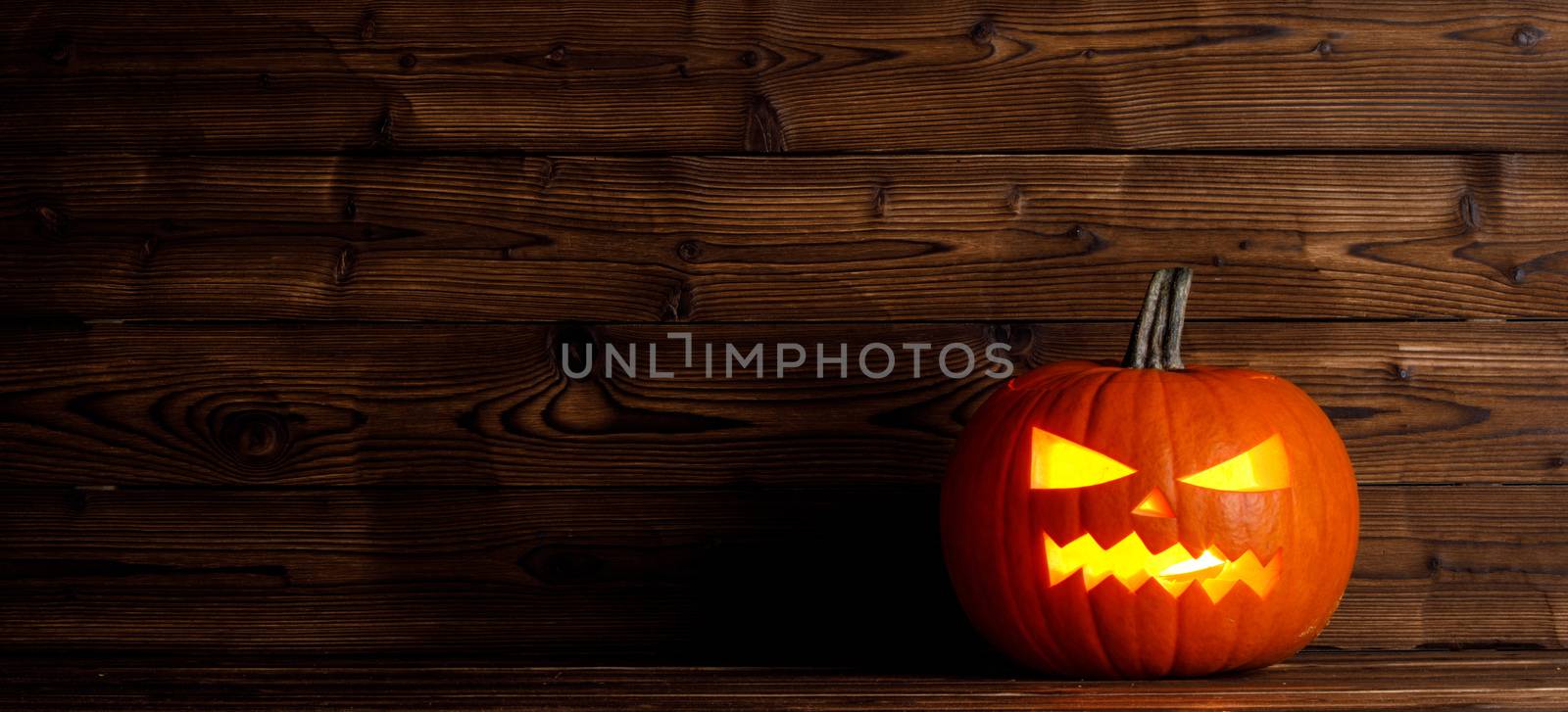 Glowing Halloween pumpkin head jack lantern on wooden background
