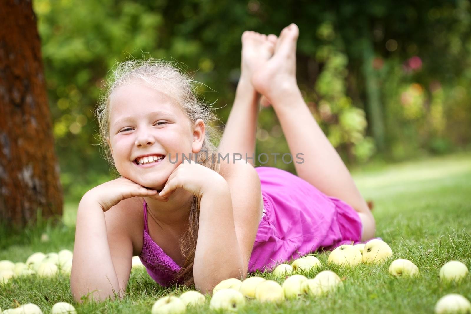 Cute young girl with stack of green fresh apples in the garden