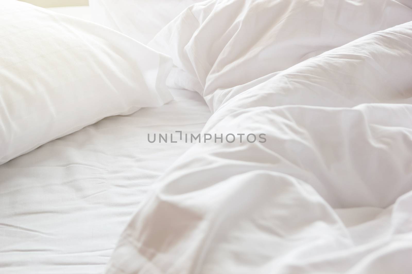 wrinkle messy blanket and white pillow in bedroom after waking up in the morning, from sleeping in a long night, details of duvet and blanket, an unmade bed in hotel bedroom with white blanket.