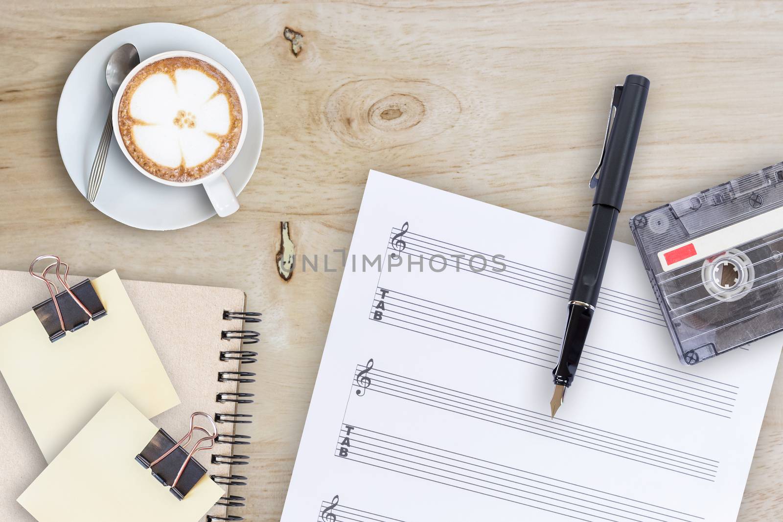 Sheet music, fountain pen, tape cassette and coffee latte on wooden table, top view picture