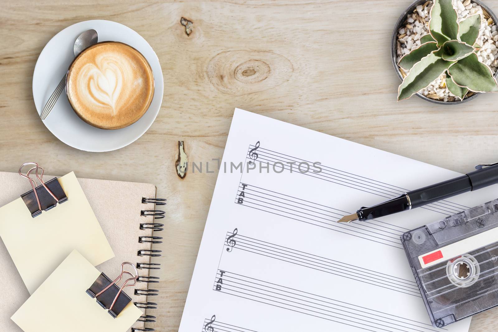 Sheet music, cactus, fountain pen, tape cassette and coffee latte on wooden table, top view picture